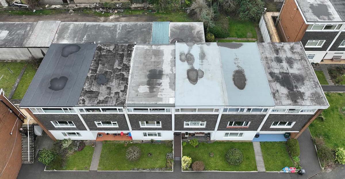 Top-down view of a house featuring a roof covered in dirt, set against a backdrop of trees and open land.