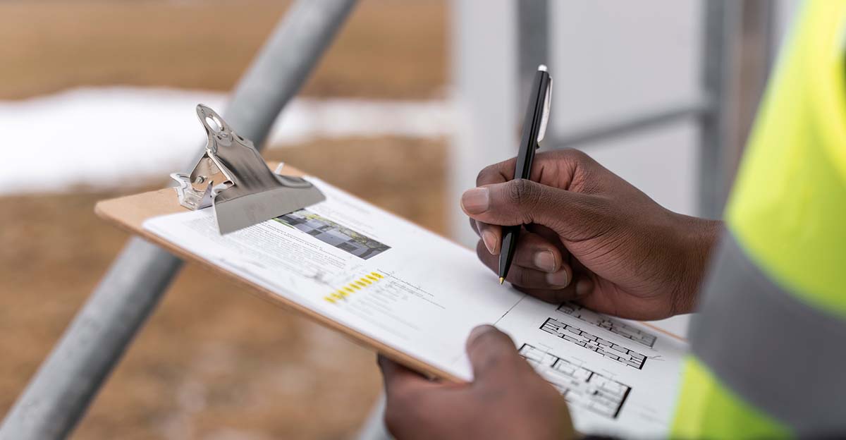 A man wearing a safety vest is taking notes on a clipboard