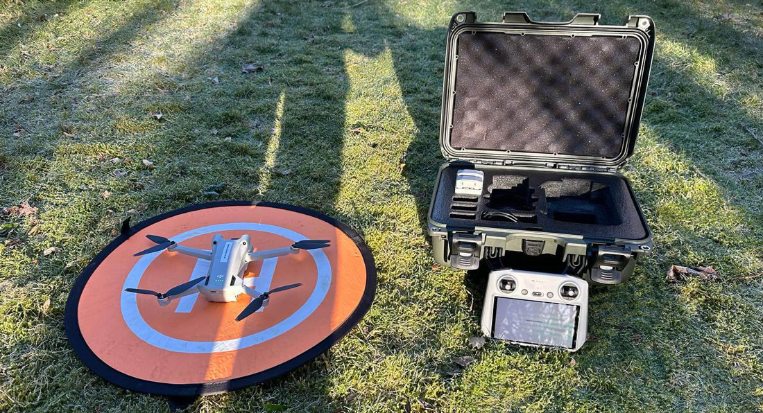 A drone with a protective case rests on the grass.  