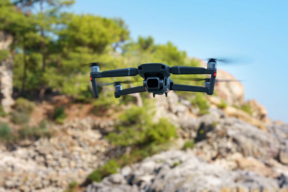 A black drone soaring above a rugged, rocky landscape, capturing aerial views of the terrain below.