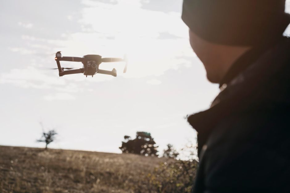 A man operates a drone above a vast green field, showcasing the technology in an outdoor setting.