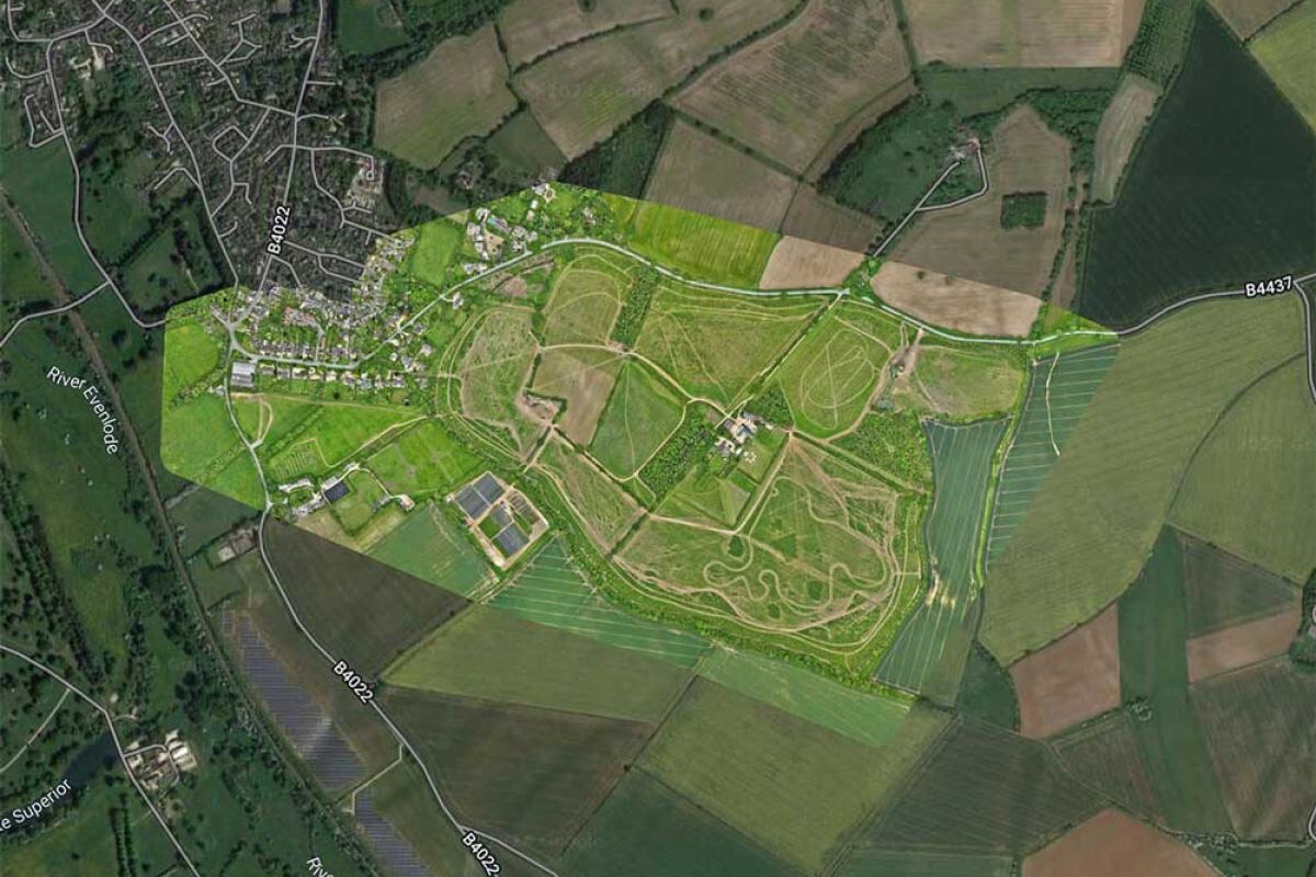 Aerial view of a lush green field featuring a road and a green building amidst the landscape. 