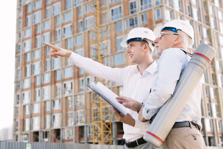 Two men in hard hats are pointing at an object, discussing details on a construction site.