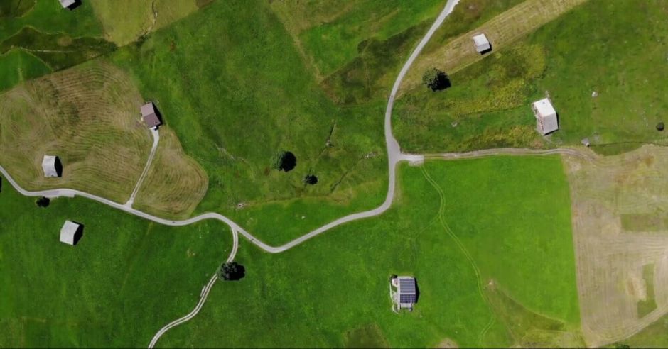 Aerial view of a lush countryside farm, showcasing fields, barns, and winding paths under a clear blue sky